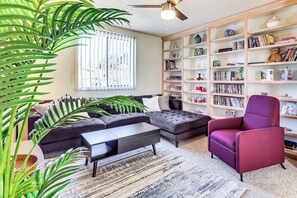 A living room with a sectional sofa, a coffee table, a purple armchair, and a bookshelf filled with books and decorative items.