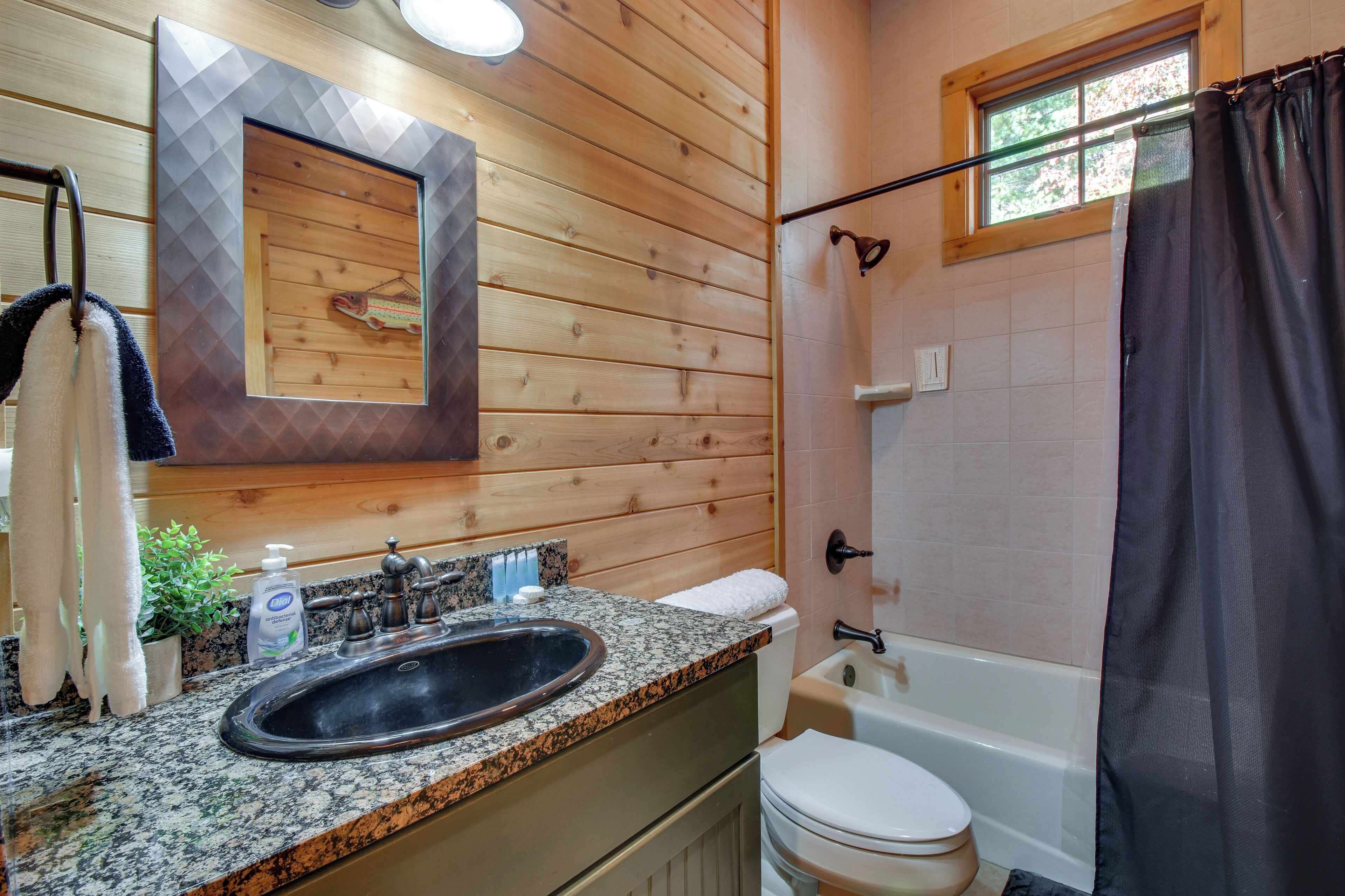 A bathroom with a wooden wall, a granite sink, a toilet, and a bathtub.