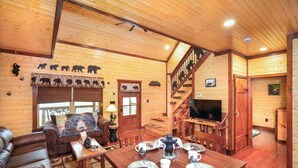 A wooden cabin interior with a dining area, sofa, and staircase. - BEARLY LIVIN!  NEW CABIN ON 2 ACRES OF PRIVATE SMOKIES TROUT STREAM!  WOW !! (Cosby)