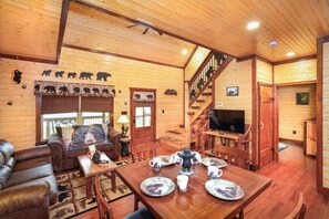 A wooden cabin interior with a dining area, sofa, and staircase. - BEARLY LIVIN!  NEW CABIN ON 2 ACRES OF PRIVATE SMOKIES TROUT STREAM!  WOW !! (Cosby)