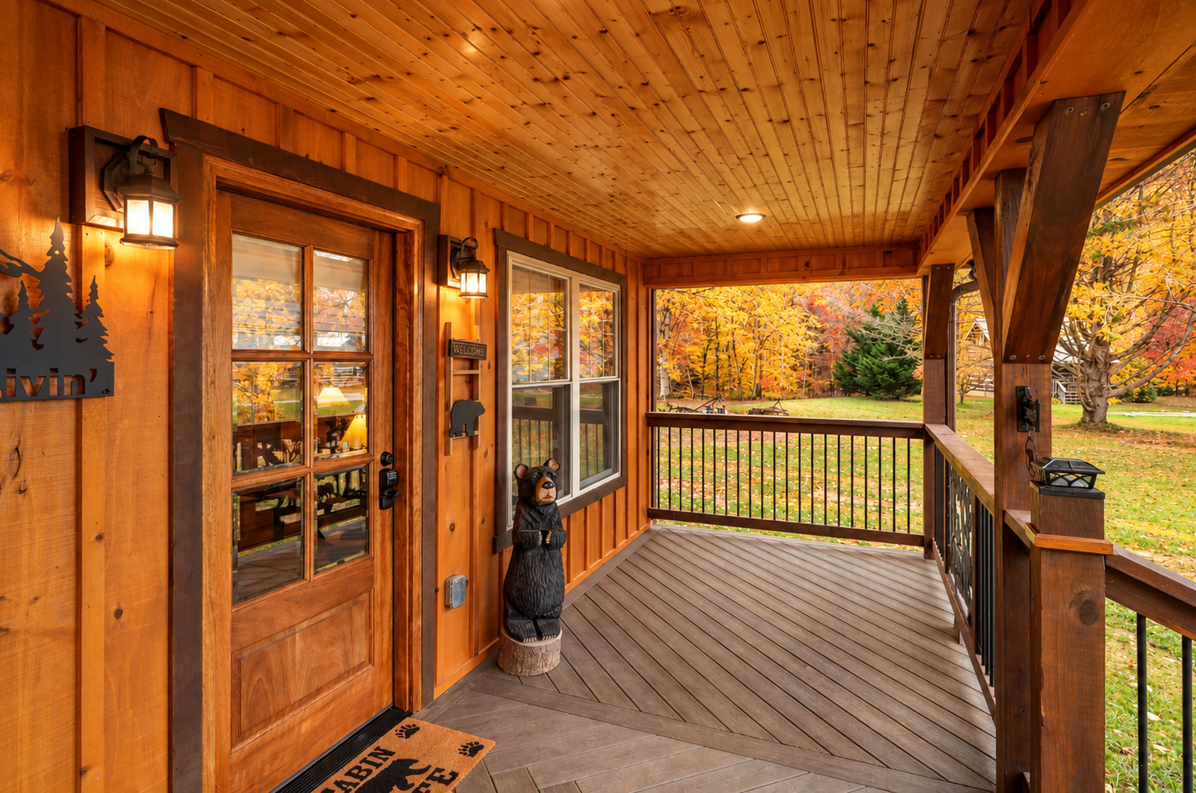 Een houten cabinentree met een veranda, een bord met een welkomstboodschap en een beerbeeld.