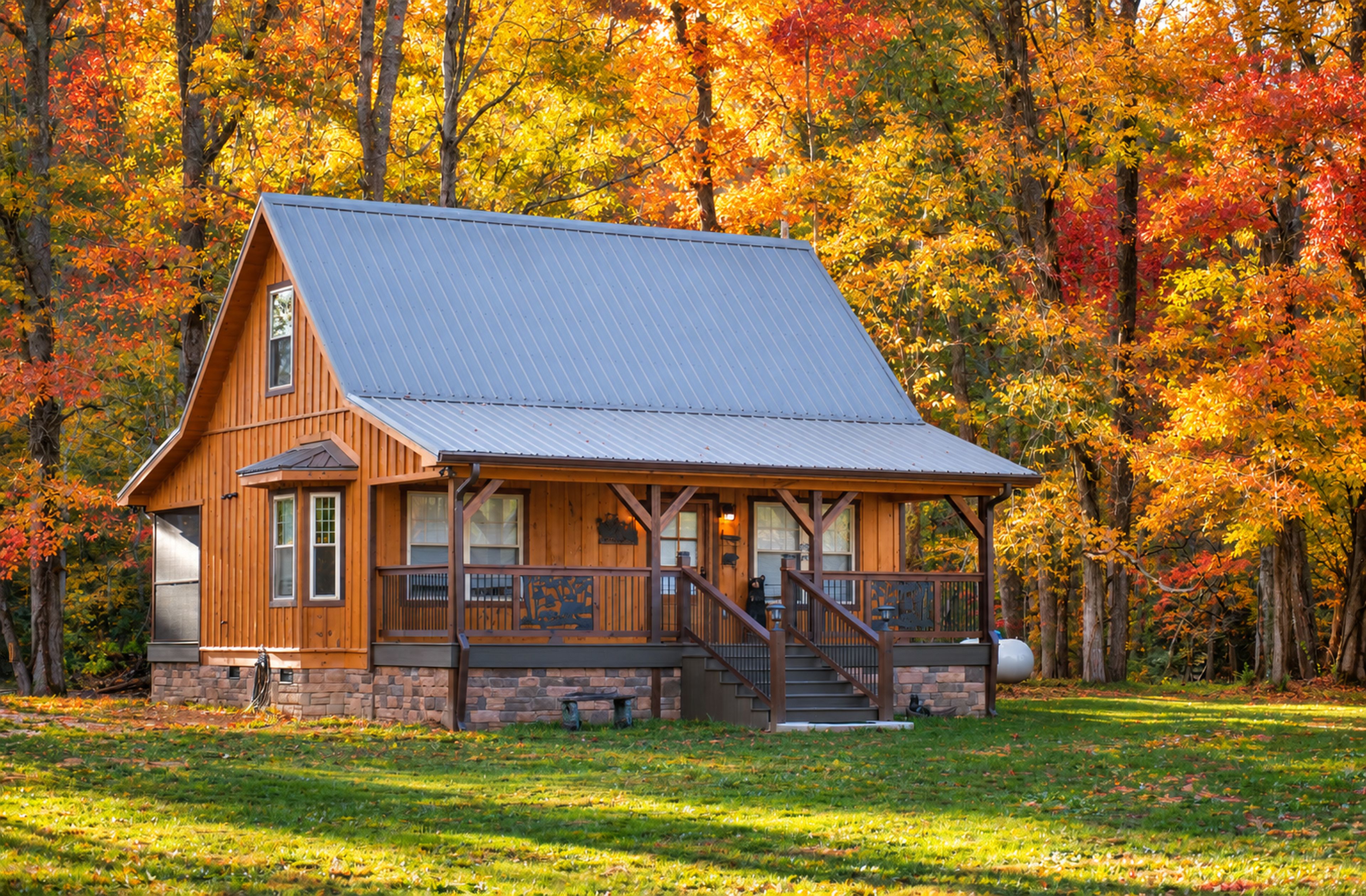 A cabin with a sloped roof, wooden exterior, and a porch with steps leading up to it.