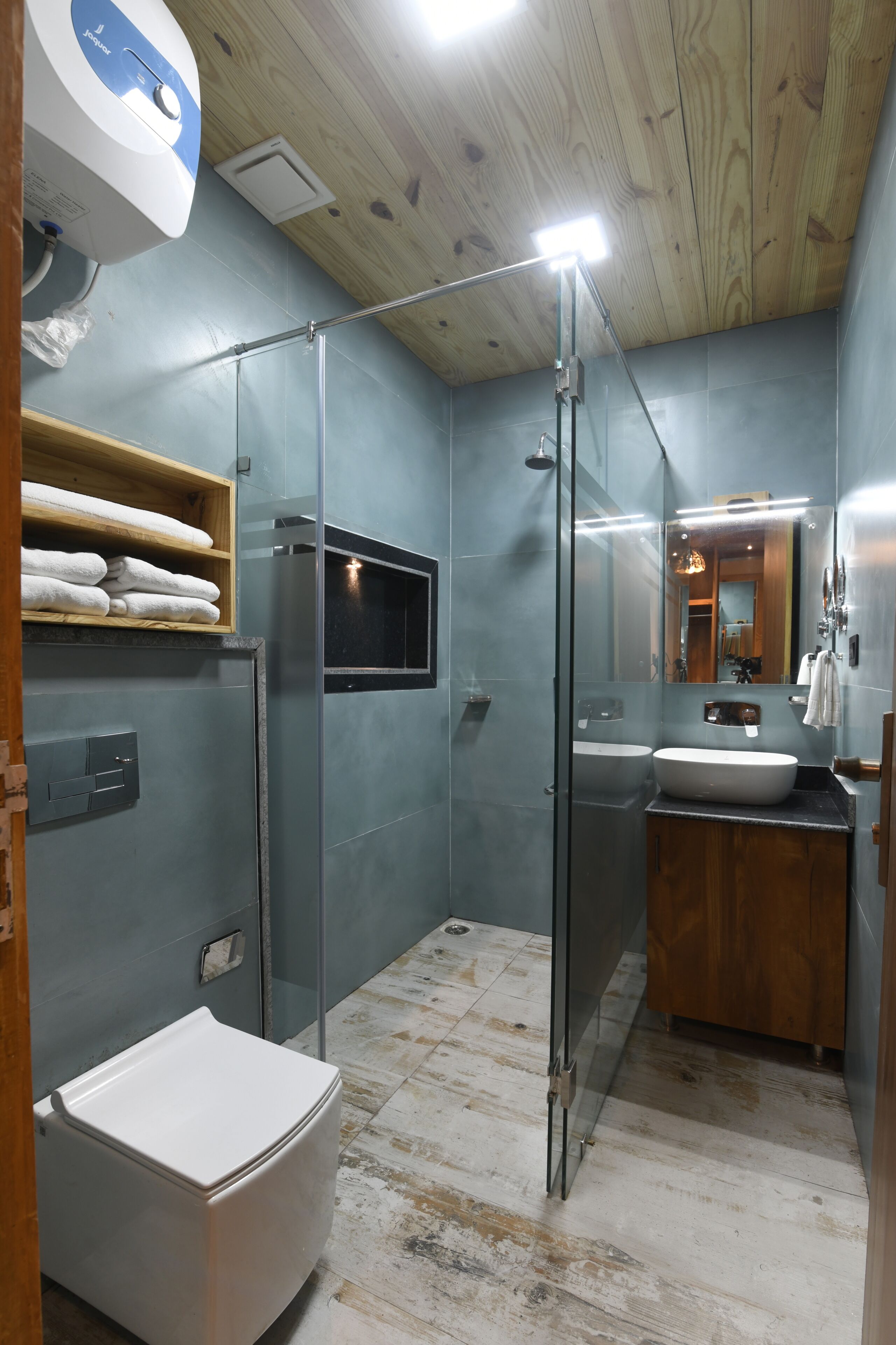 Un baño moderno con cabina de ducha de vidrio, un inodoro blanco, un lavabo con tocador de madera y un espejo sobre el lavabo.