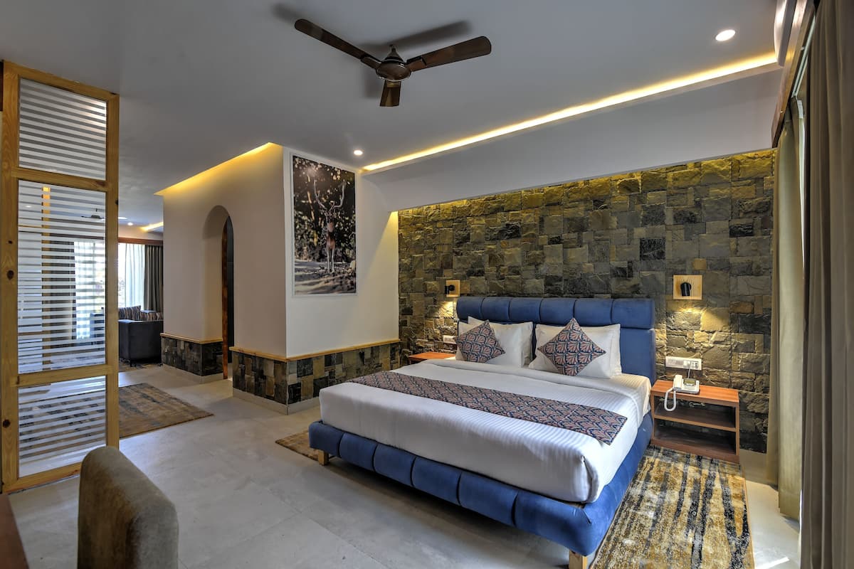 A bedroom with a stone wall, a ceiling fan, a bed with blue bedding, and a nightstand with a lamp.