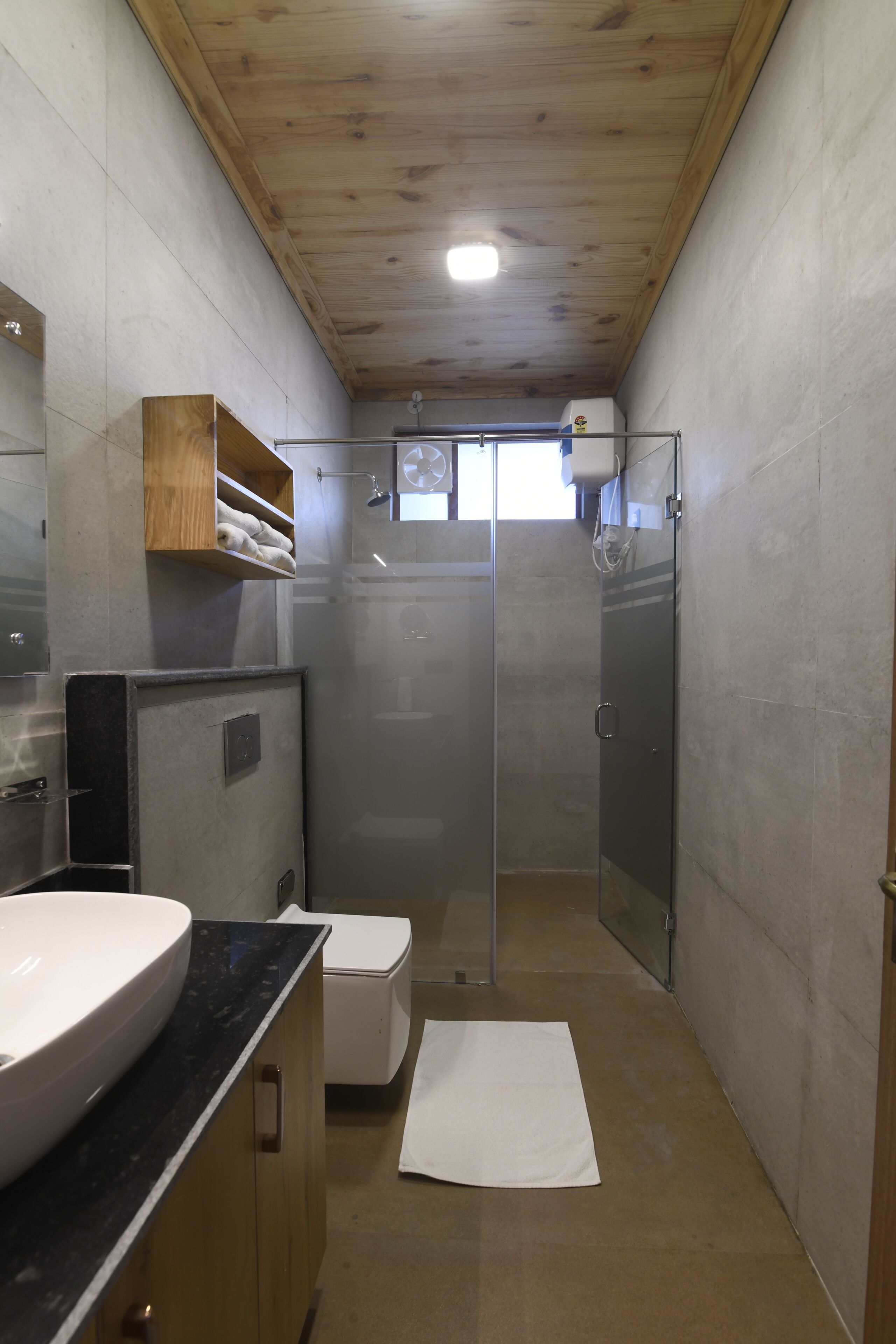 Un baño con techo de madera, un lavamanos grande, un inodoro y una ducha con cerramiento de vidrio.