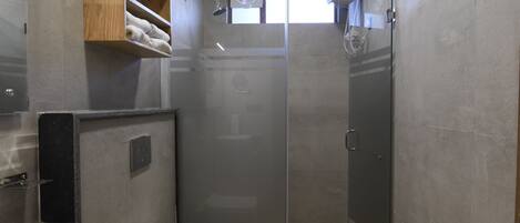 A bathroom with a wooden ceiling, a large sink, a toilet, and a glass-enclosed shower.