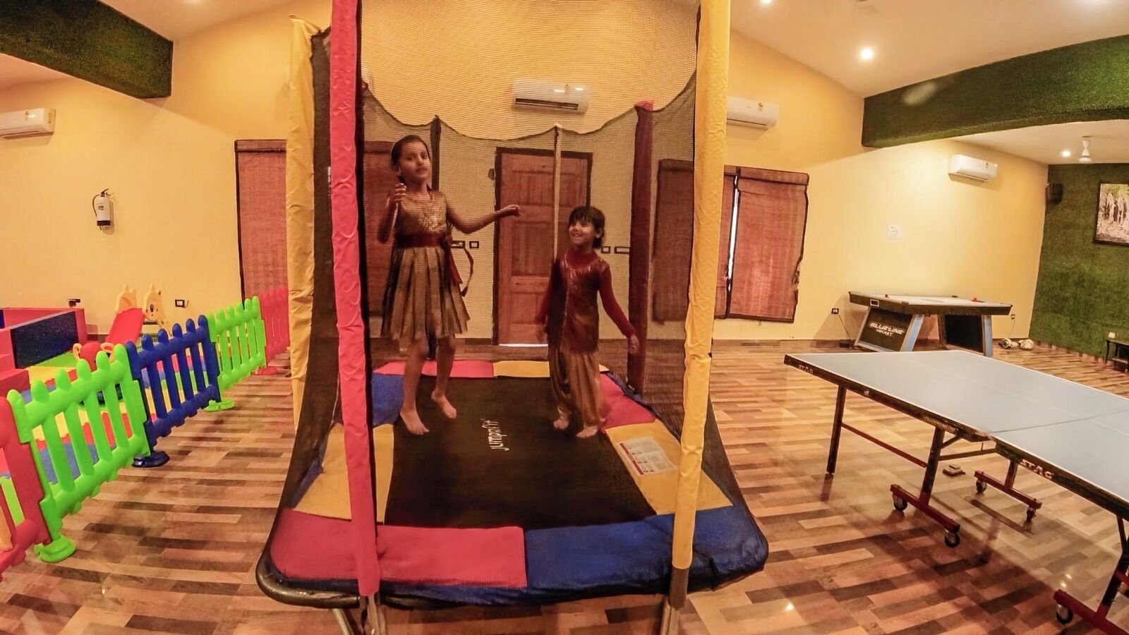 Una habitación con trampolín, mesa de ping pong y zona de juegos con barreras de colores.