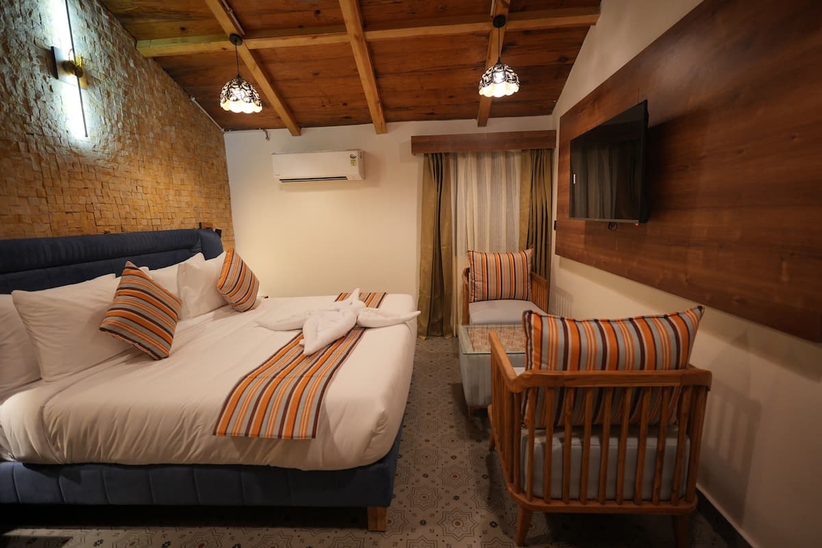 A hotel room with a bed, a chair, a TV, an air conditioner, and a wooden ceiling.