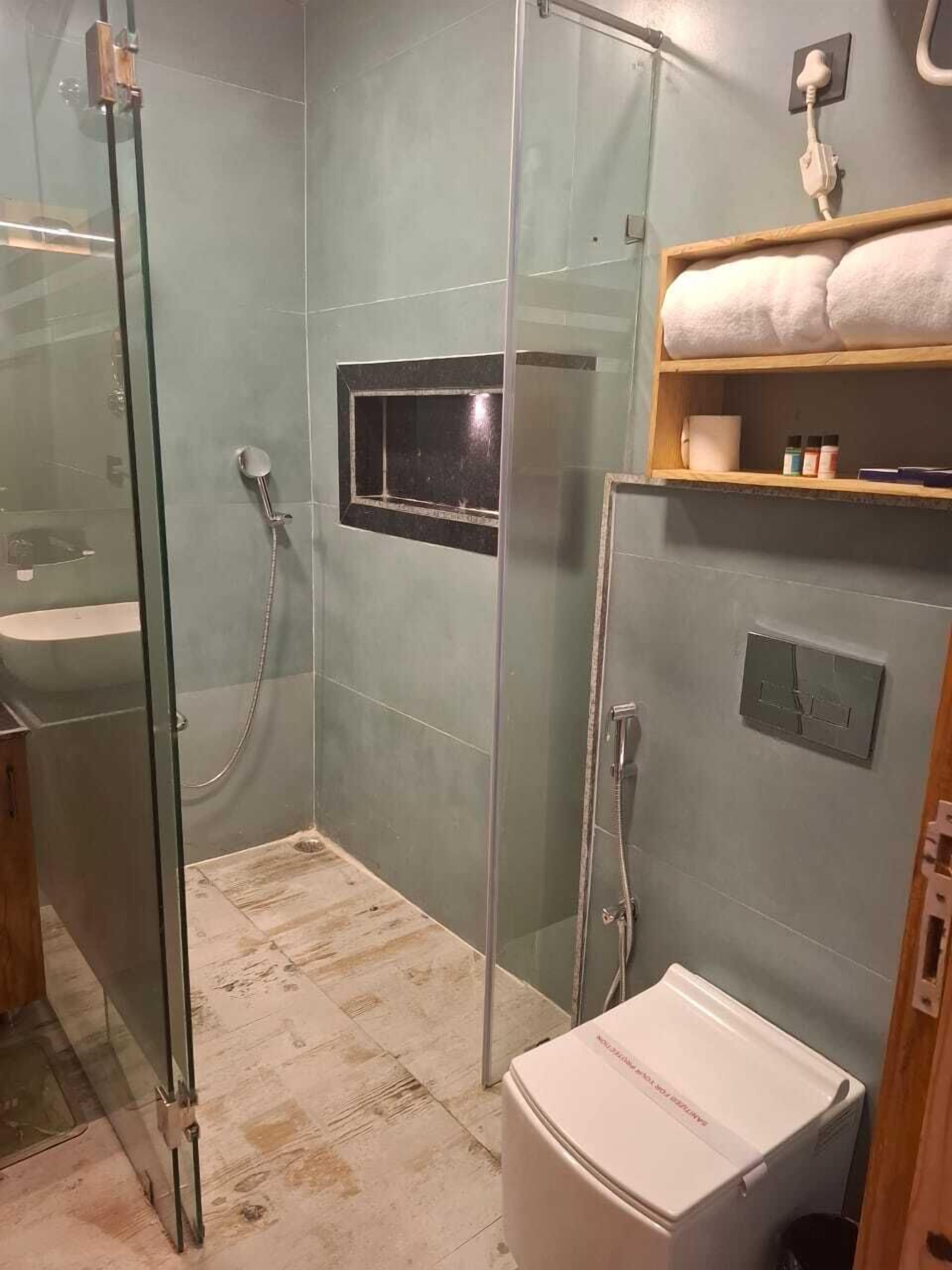 Ein Badezimmer mit einer Duschkabine, einer weißen Toilette, einem Waschbecken und einem Regal mit Handtüchern und Pflegeprodukten.