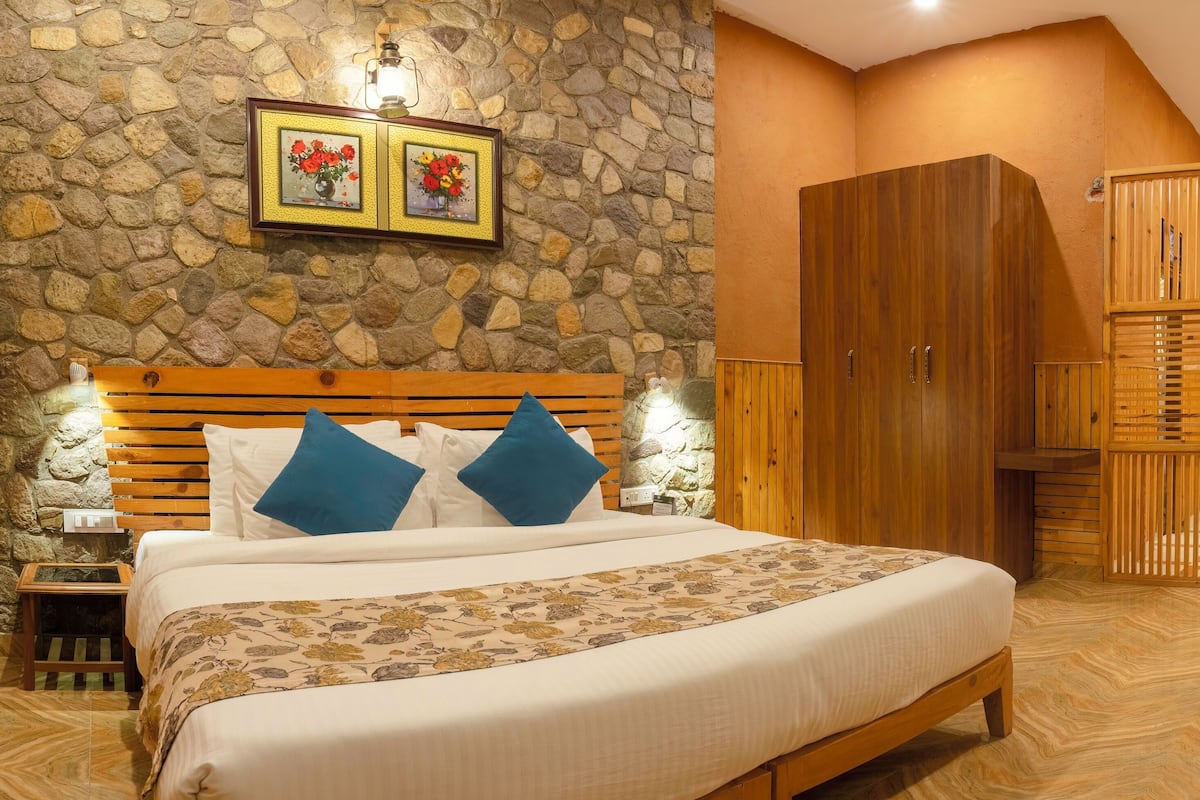 A hotel room with a stone wall, wooden bed, and a wardrobe.