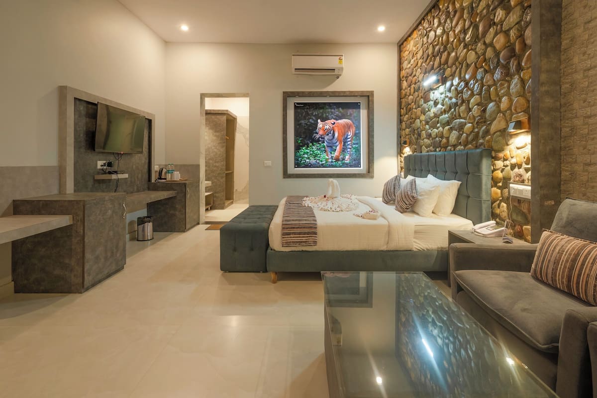 A modern bedroom with a bed, a sofa, a TV, and a stone wall.