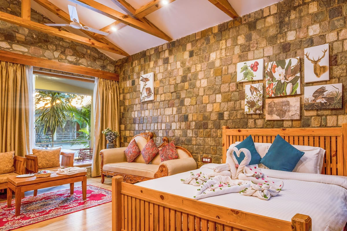 A hotel room with a stone wall, wooden furniture, a bed with towels, and artwork on the wall.