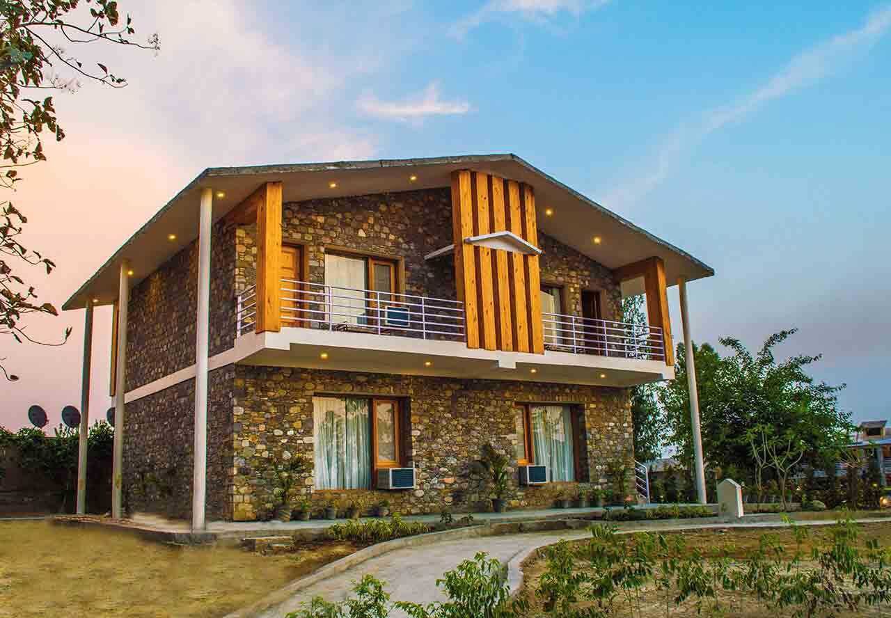 A two-story house with a stone facade, a balcony with a railing, and a small garden area in front.
