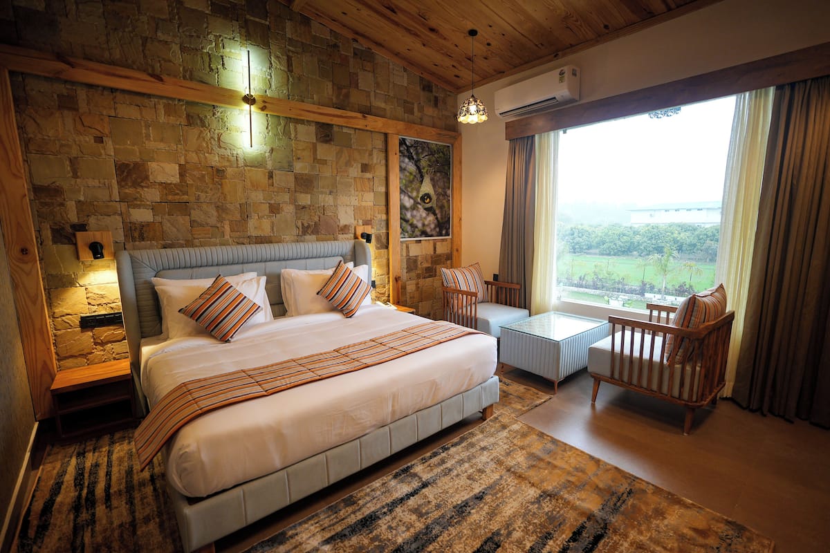 A bedroom with a stone wall, a bed, a chair, a table, and a window with a view.