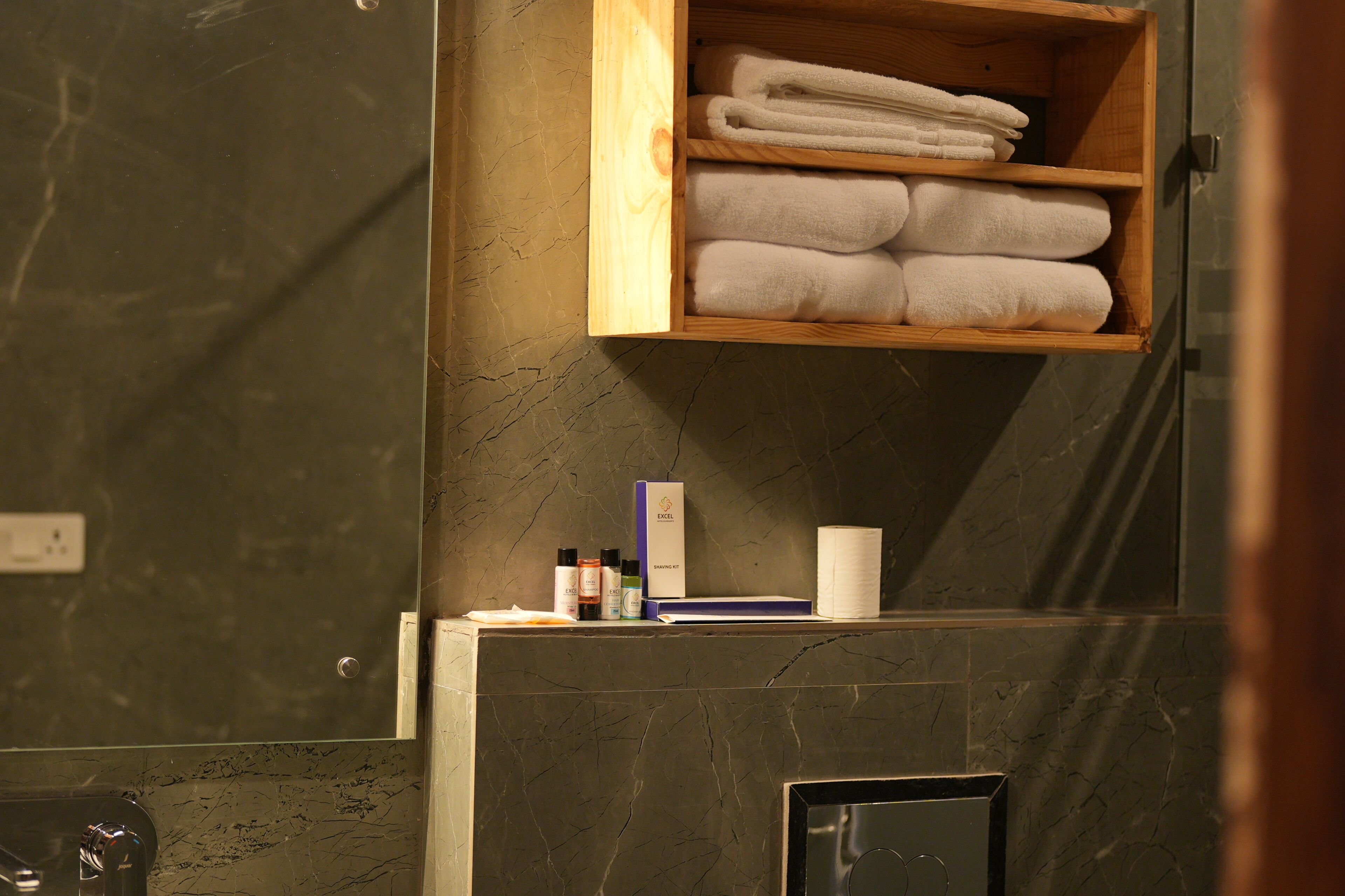 A bathroom with a wooden shelf holding folded towels, a mirror, and toiletries.