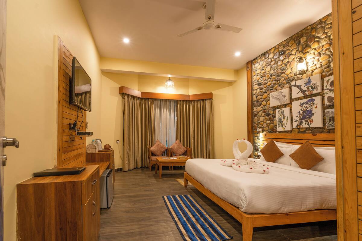 A hotel room with a wooden bed, a desk with a chair, a television mounted on the wall, and a stone wall with artwork.