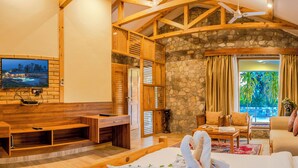 A spacious living area with a stone wall, wooden furniture, a flat-screen TV, and a view of the outdoors. - The Banyan Retreat by Excel Hotels & Resorts (Ramnagar)