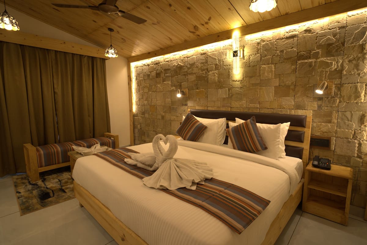 A hotel room with a large bed, wooden headboard, stone wall, and a ceiling fan.