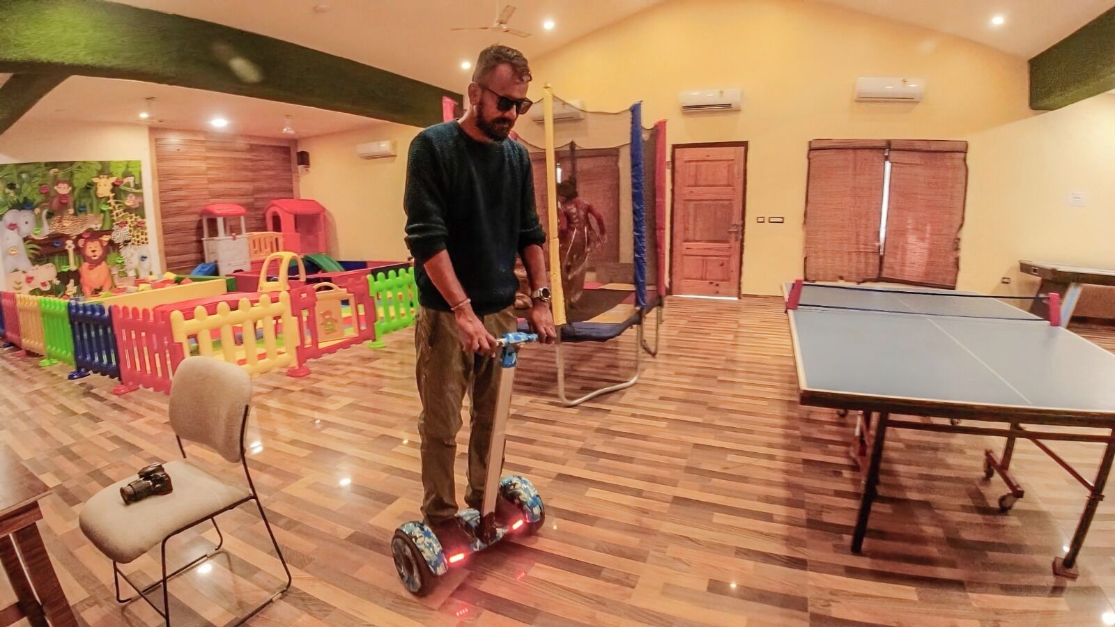 Une personne sur une planche à roulettes à lévitation dans une pièce où se trouvent une table de ping-pong, un plancher en bois et des structures de jeu colorées.