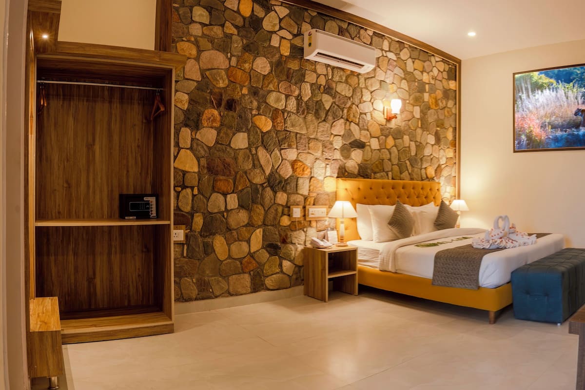 A bedroom with a stone wall, a bed with a headboard, bedside lamps, a nightstand, a wooden wardrobe, and a painting on the wall.