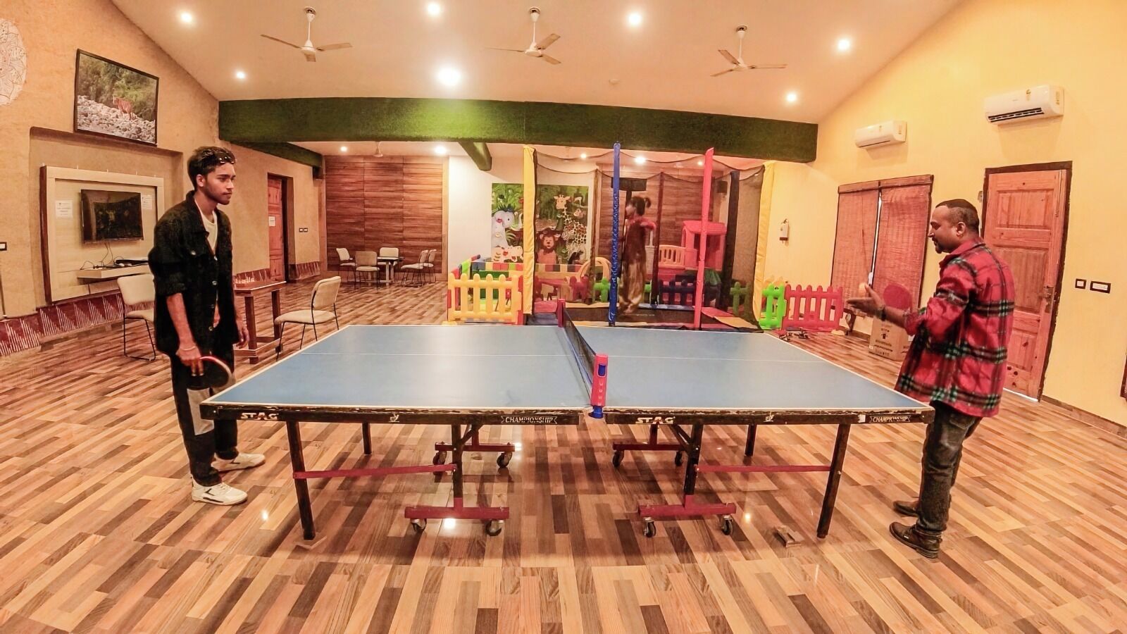 A room with a ping pong table, chairs, and a play area with colorful toys.