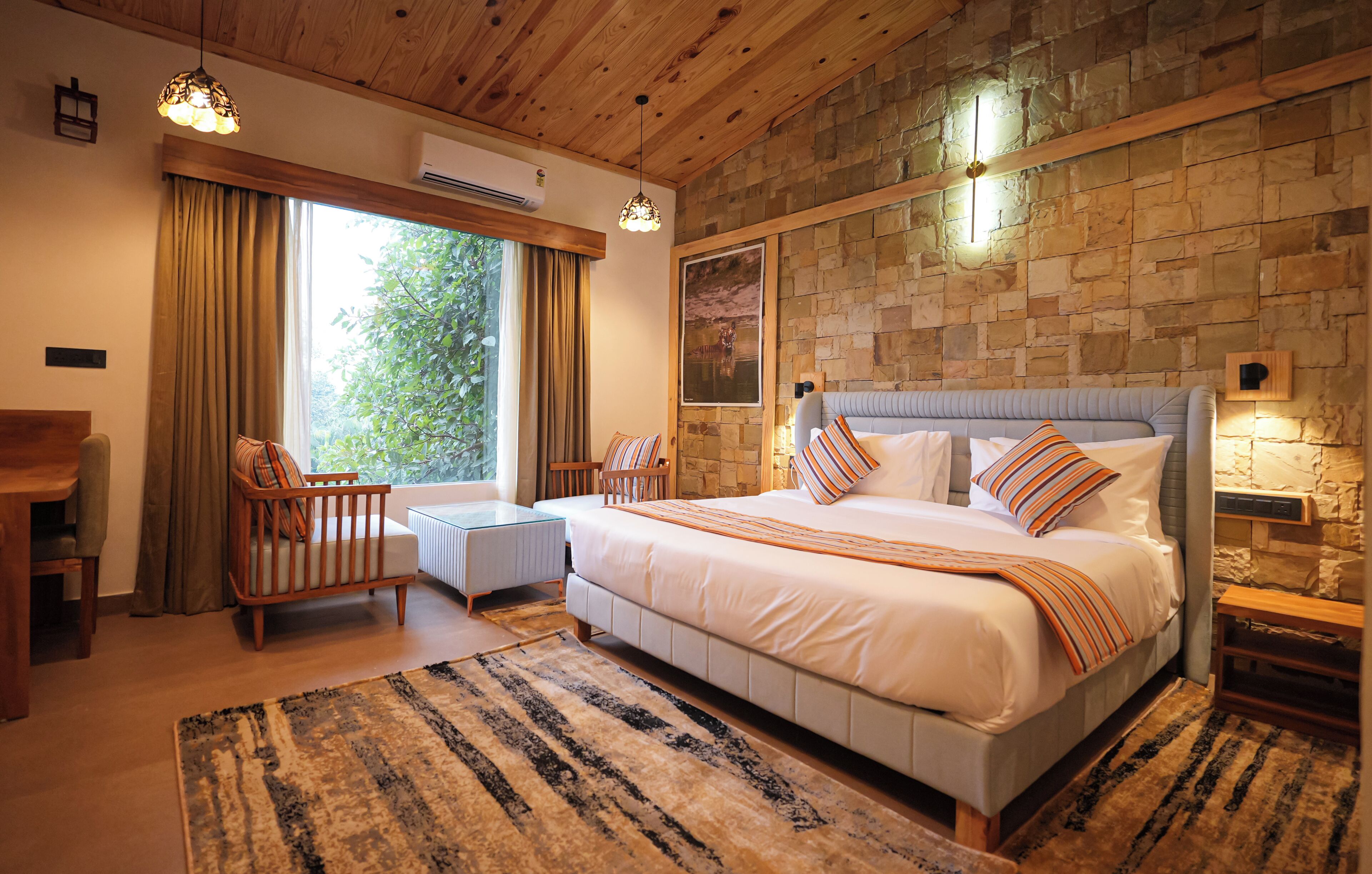 Une chambre avec un grand lit, une tête de lit en bois, un mur en pierre, une fenêtre avec des rideaux, une petite table et une chaise.