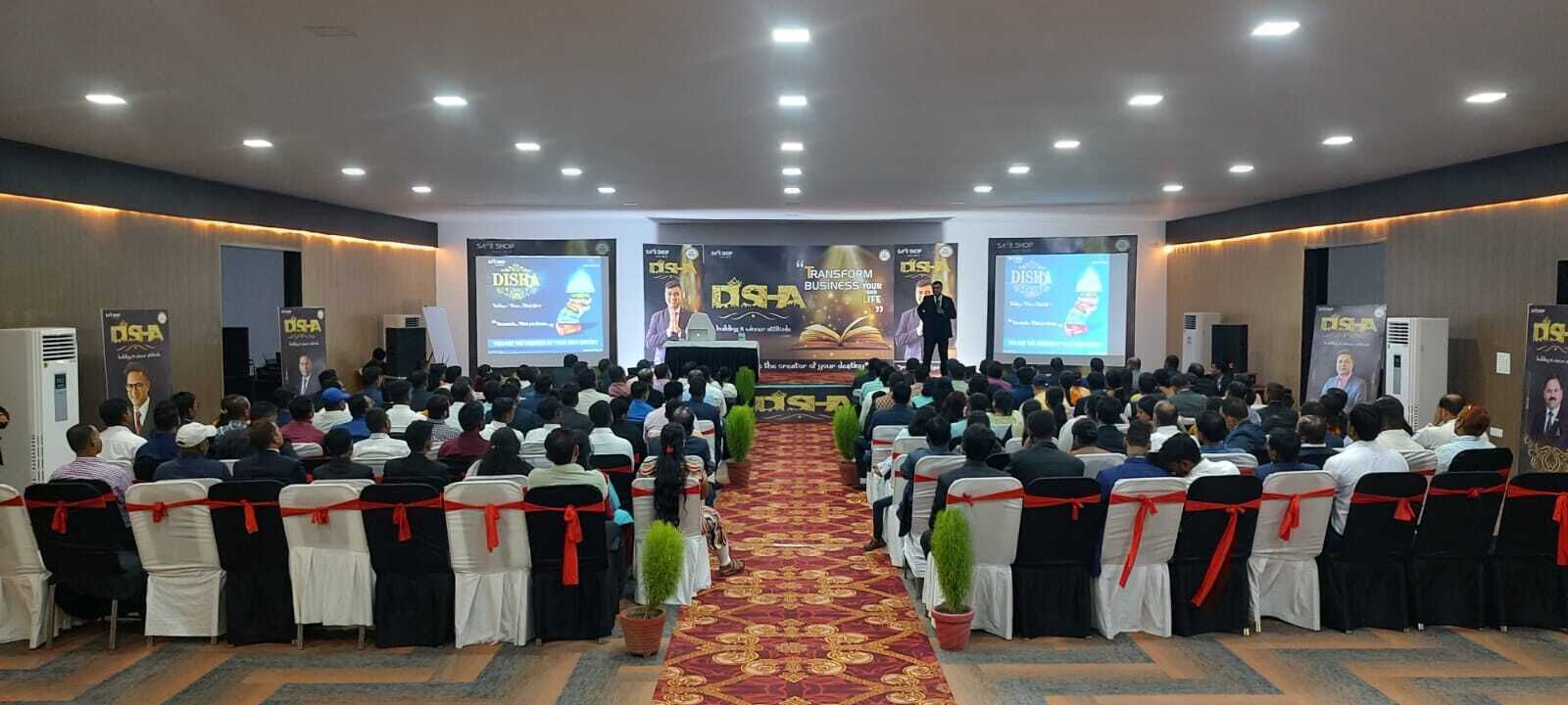A conference room with rows of chairs facing a podium, banners, and a carpeted floor.
