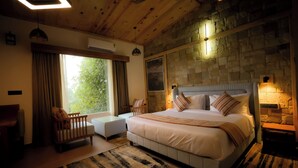 A bedroom with a large bed, a wooden ceiling, stone wall, and a view of greenery outside. - The Banyan Retreat by Excel Hotels & Resorts (Ramnagar)