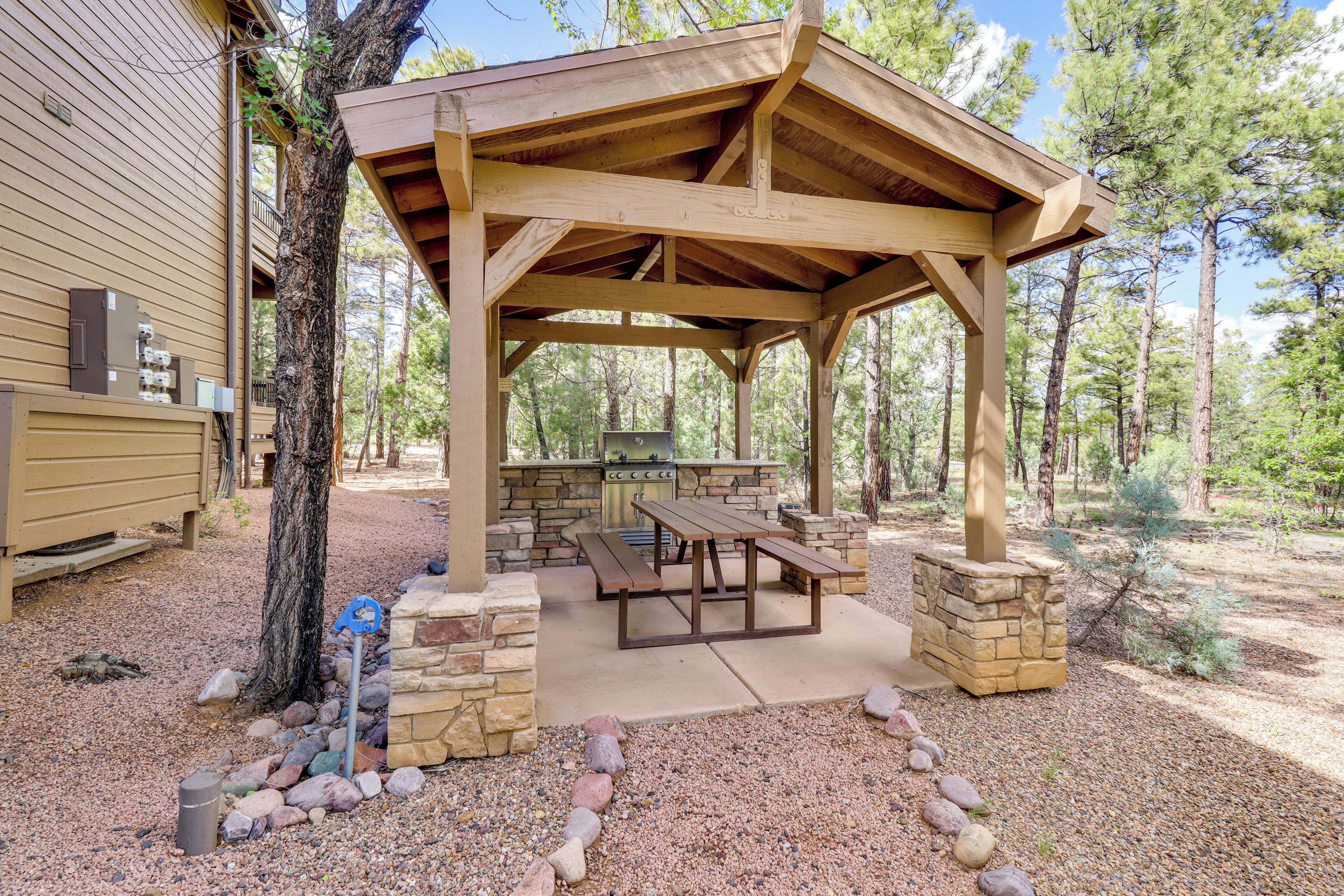 Un pavillon extérieur en bois doté d’un espace barbecue en pierre, de tables de pique-nique et d’une cheminée en pierre.