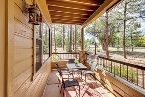 Um alpendre coberto com mesa e cadeiras, com vista para uma área arborizada.