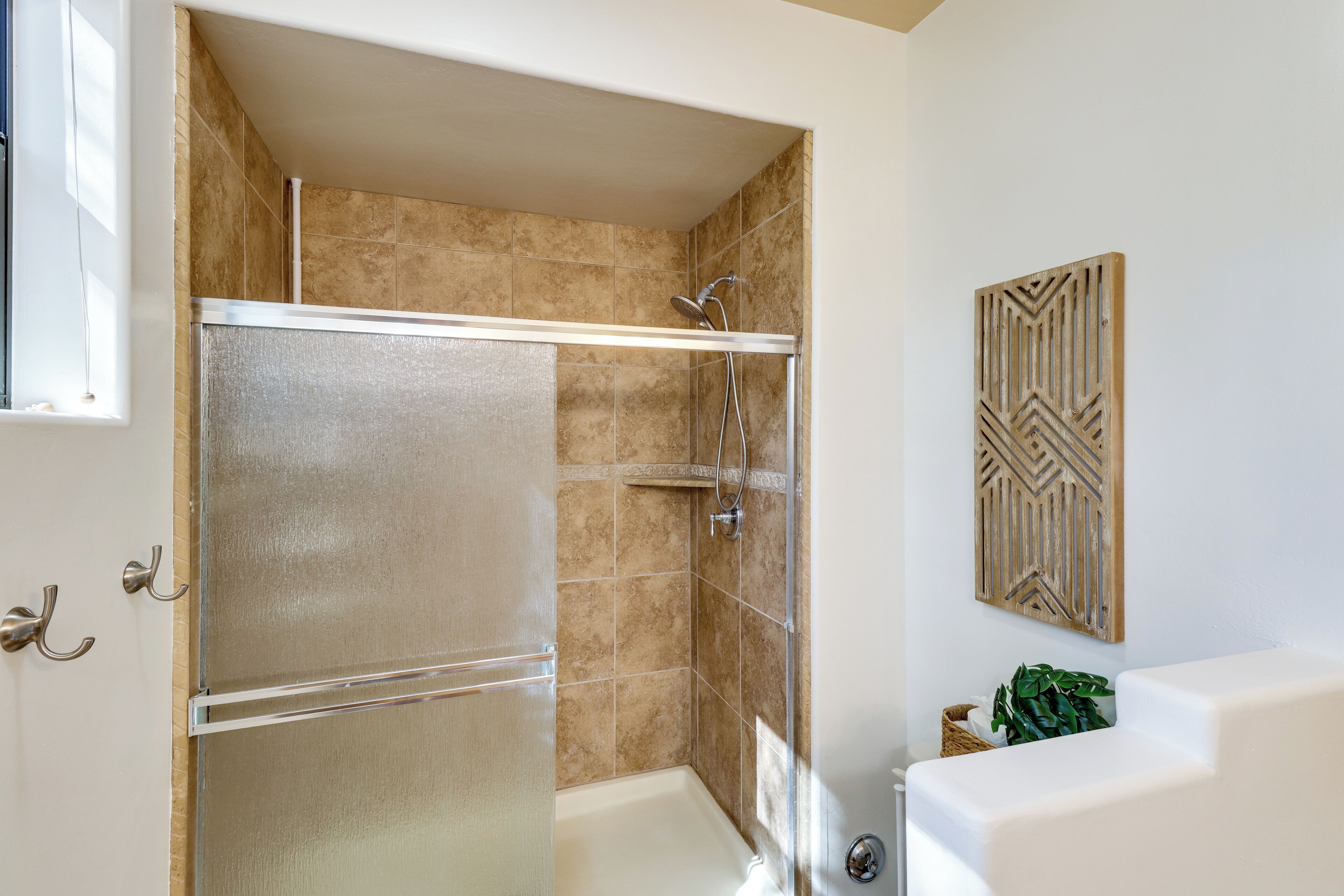 A bathroom with a glass shower enclosure, a white bathtub, and a decorative wall piece.