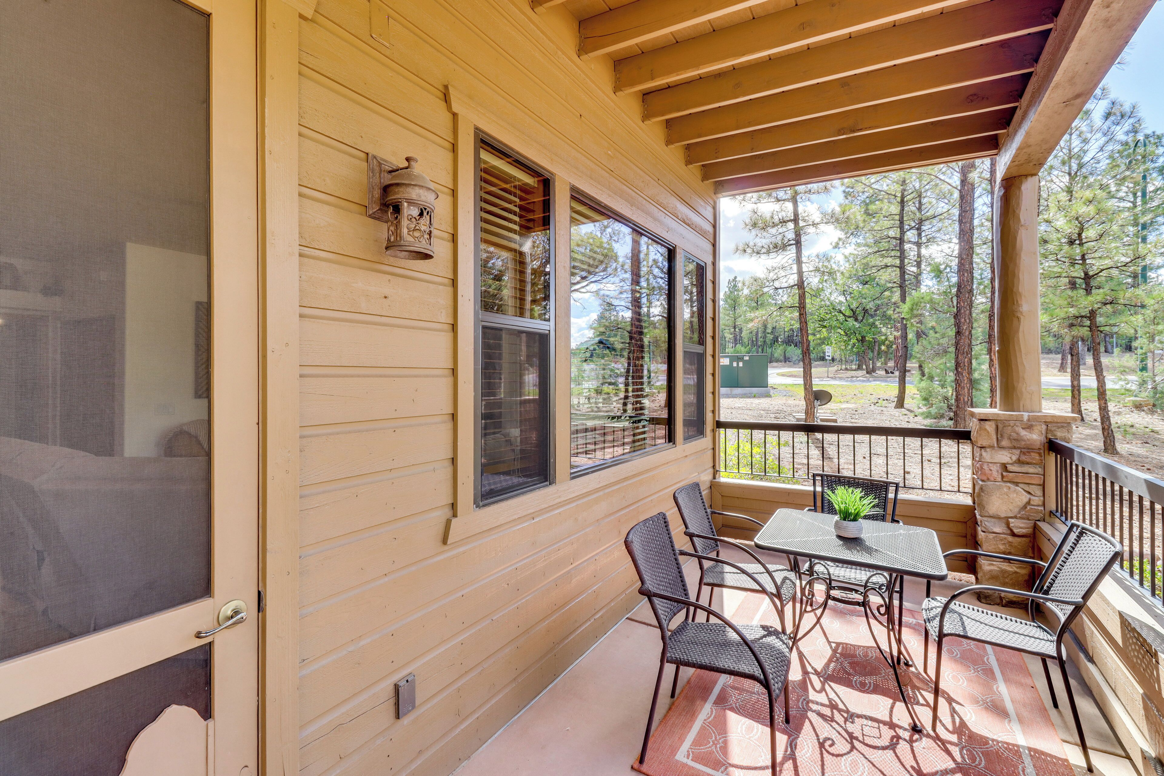 A covered porch with a table and chairs, a stone pillar, and a view of trees.