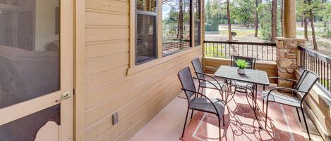 A covered porch with a table and chairs, a stone pillar, and a view of trees.