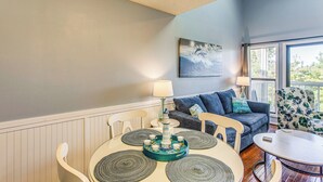 A dining area with a round table, chairs, a decorative centerpiece, a sofa, and a chair with a floral pattern. - Golf, Gamble & Deep-sea Fish: Little River Condo (Little River)