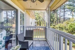 A covered porch with wicker furniture, a blue rug, and a view of a house and trees. - Golf, Gamble & Deep-sea Fish: Little River Condo (Little River)