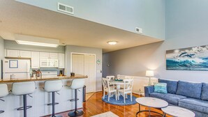 A modern kitchen with white cabinets, a bar area with stools, a dining table with chairs, and a living area with a sofa and coffee table. - Golf, Gamble & Deep-sea Fish: Little River Condo (Little River)