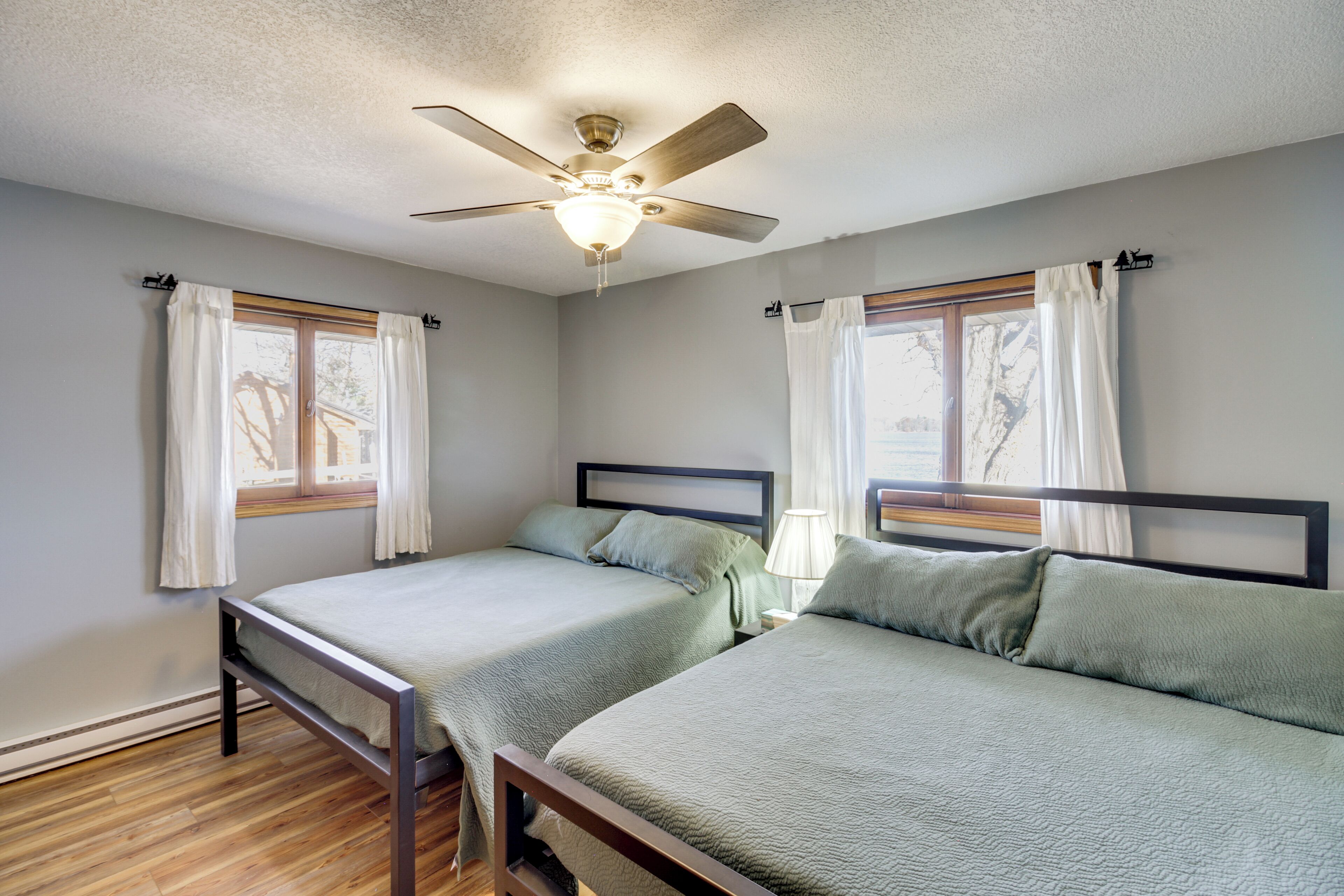 A room with two single beds, a ceiling fan, and windows with curtains.