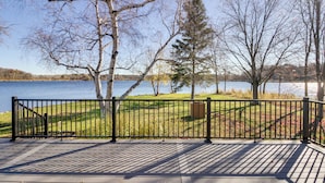 Una terraza con barandilla metálica que da a un lago, rodeada de árboles y zonas verdes.