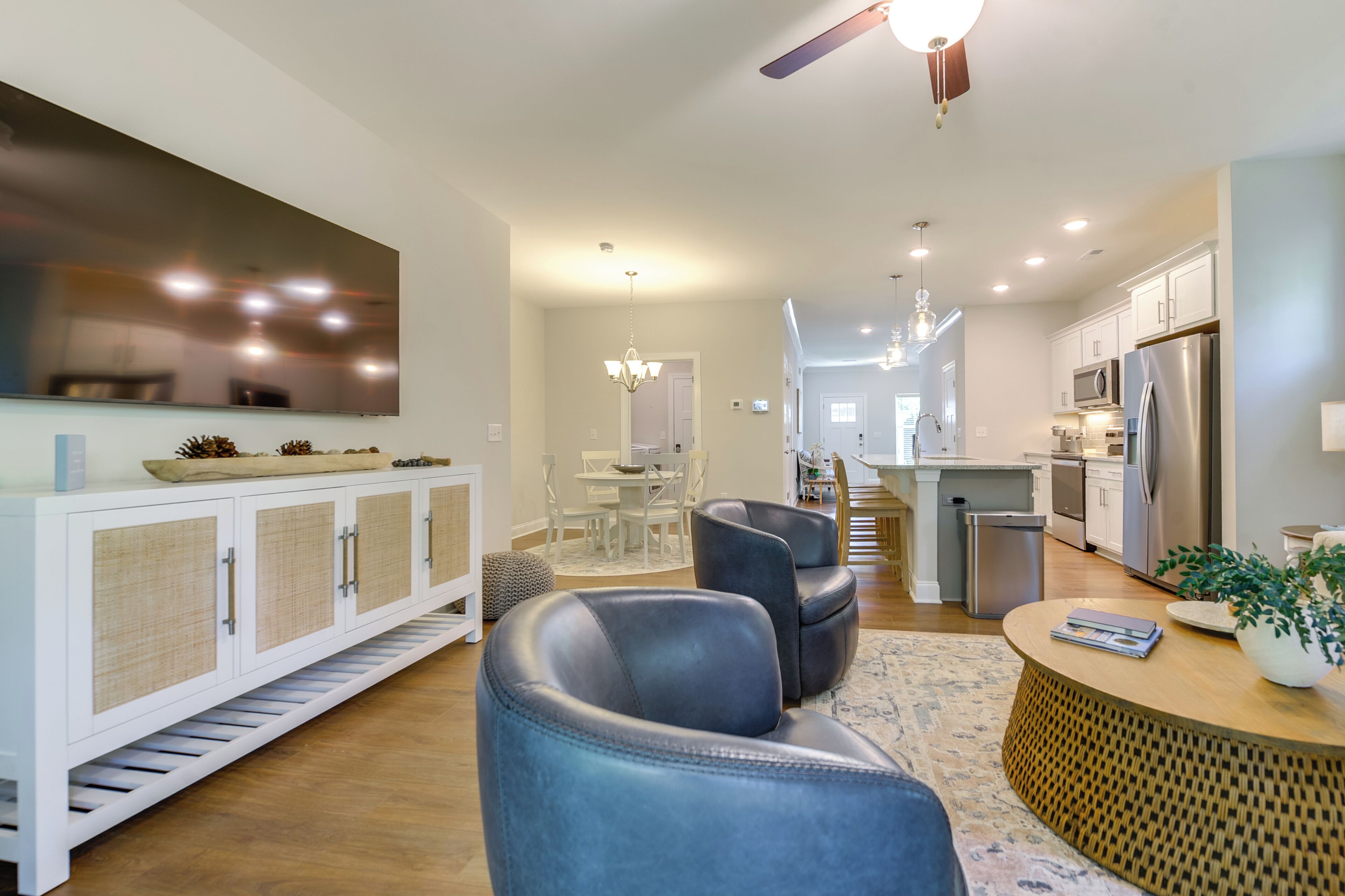 A modern kitchen with stainless steel appliances, a dining area with a white table and chairs, and a living room with a sofa and a coffee table.