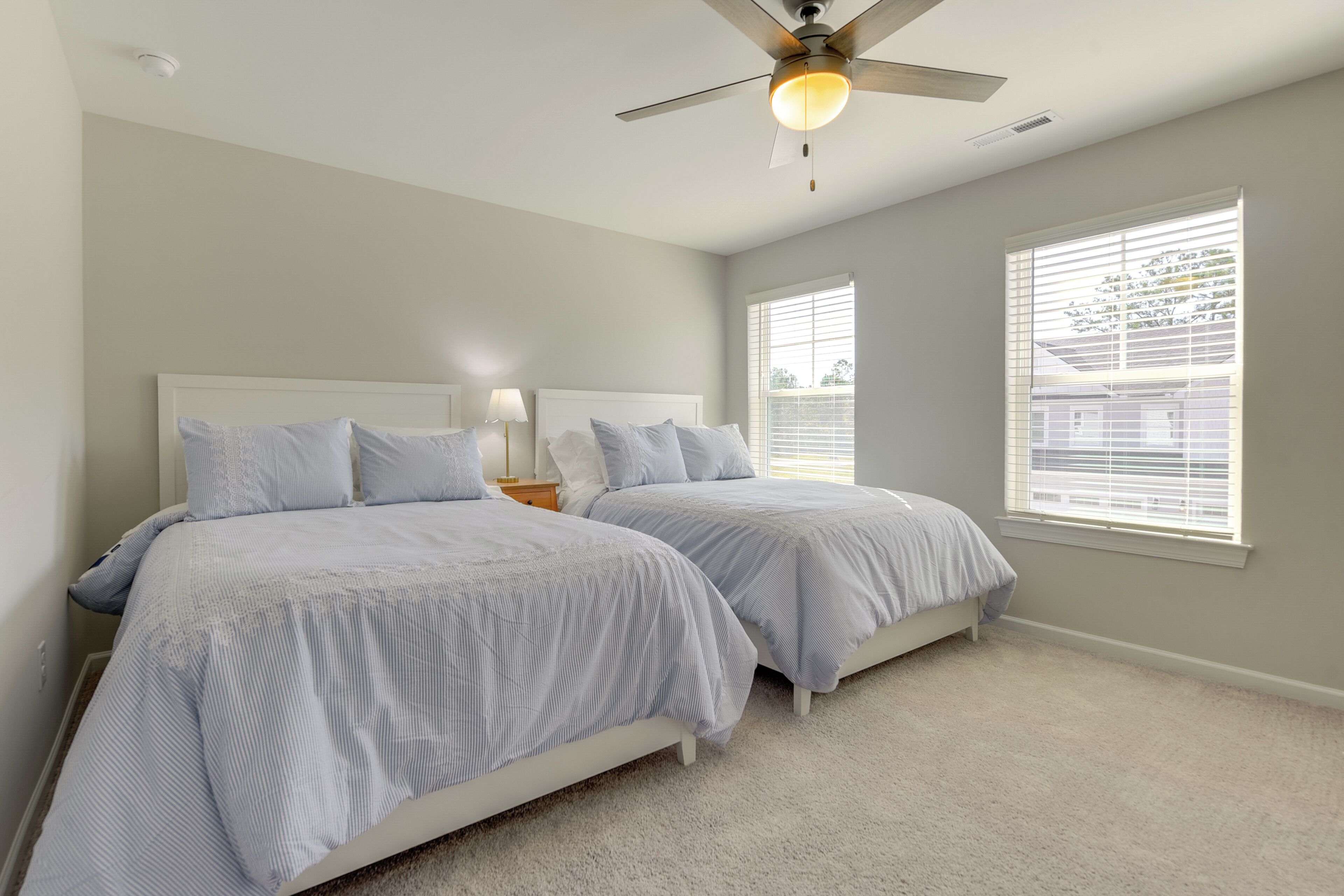 A bedroom with two beds, a ceiling fan, and large windows with blinds.