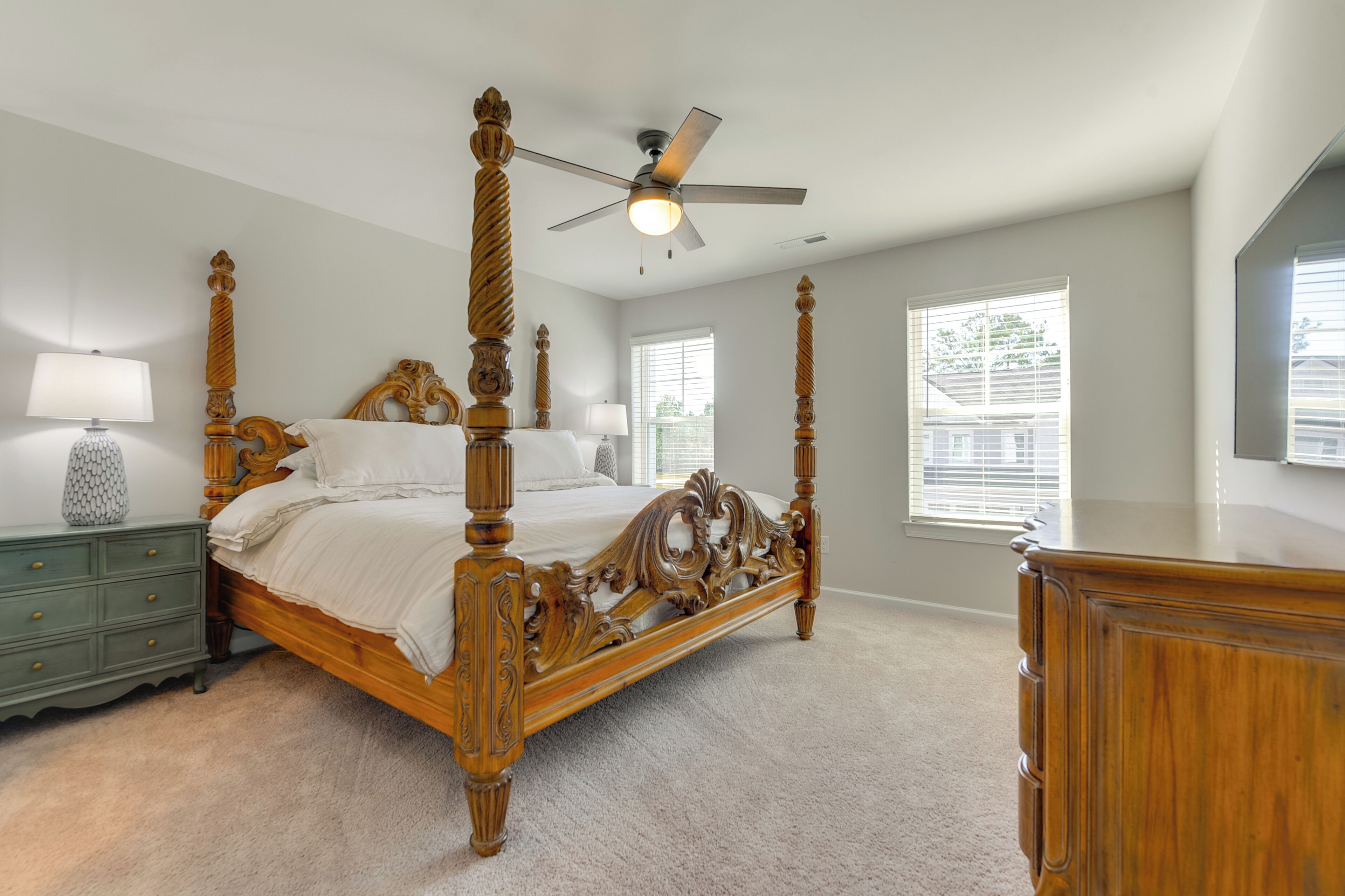 A bedroom with a four-poster bed, a ceiling fan, and a large window with blinds.