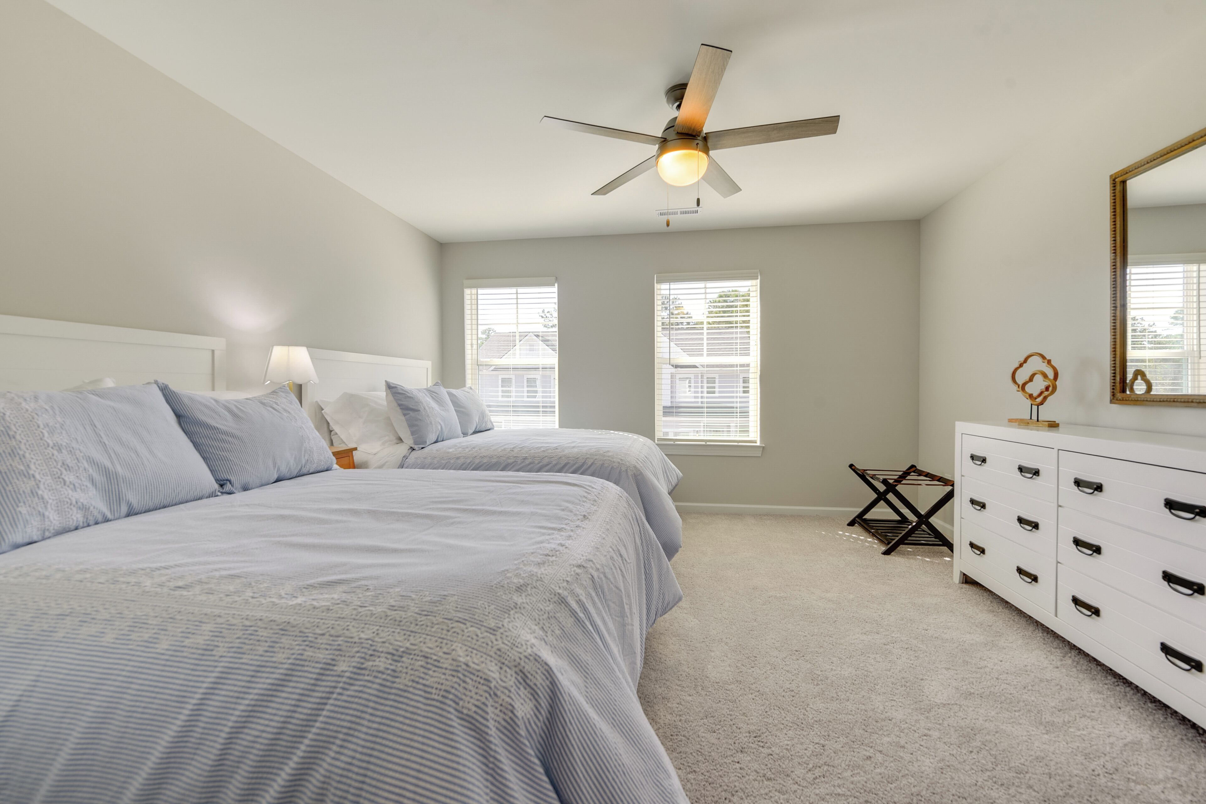A bedroom with two beds, a ceiling fan, a dresser, and a window.