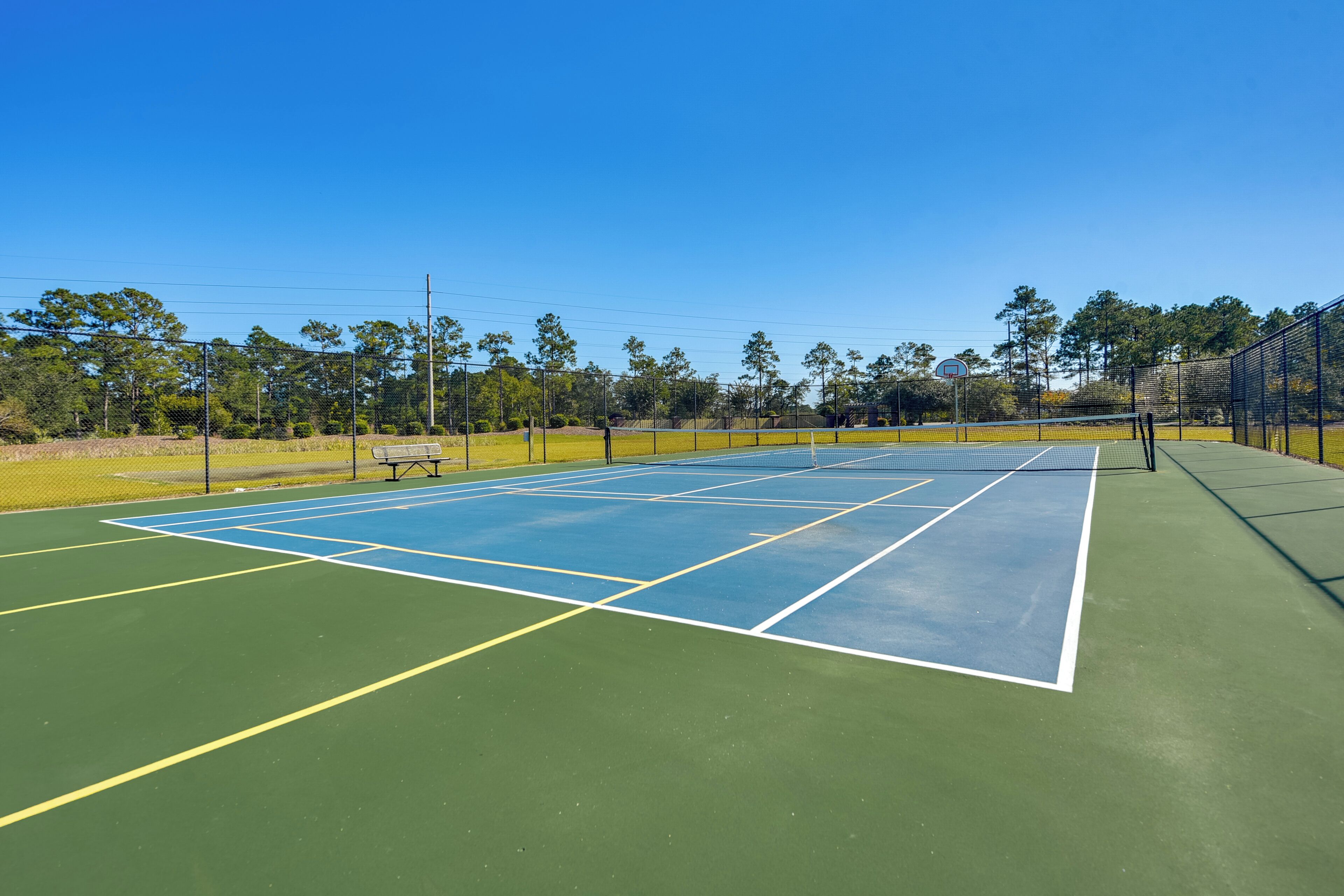 A tennis court with a net, surrounded by a fence and trees.
