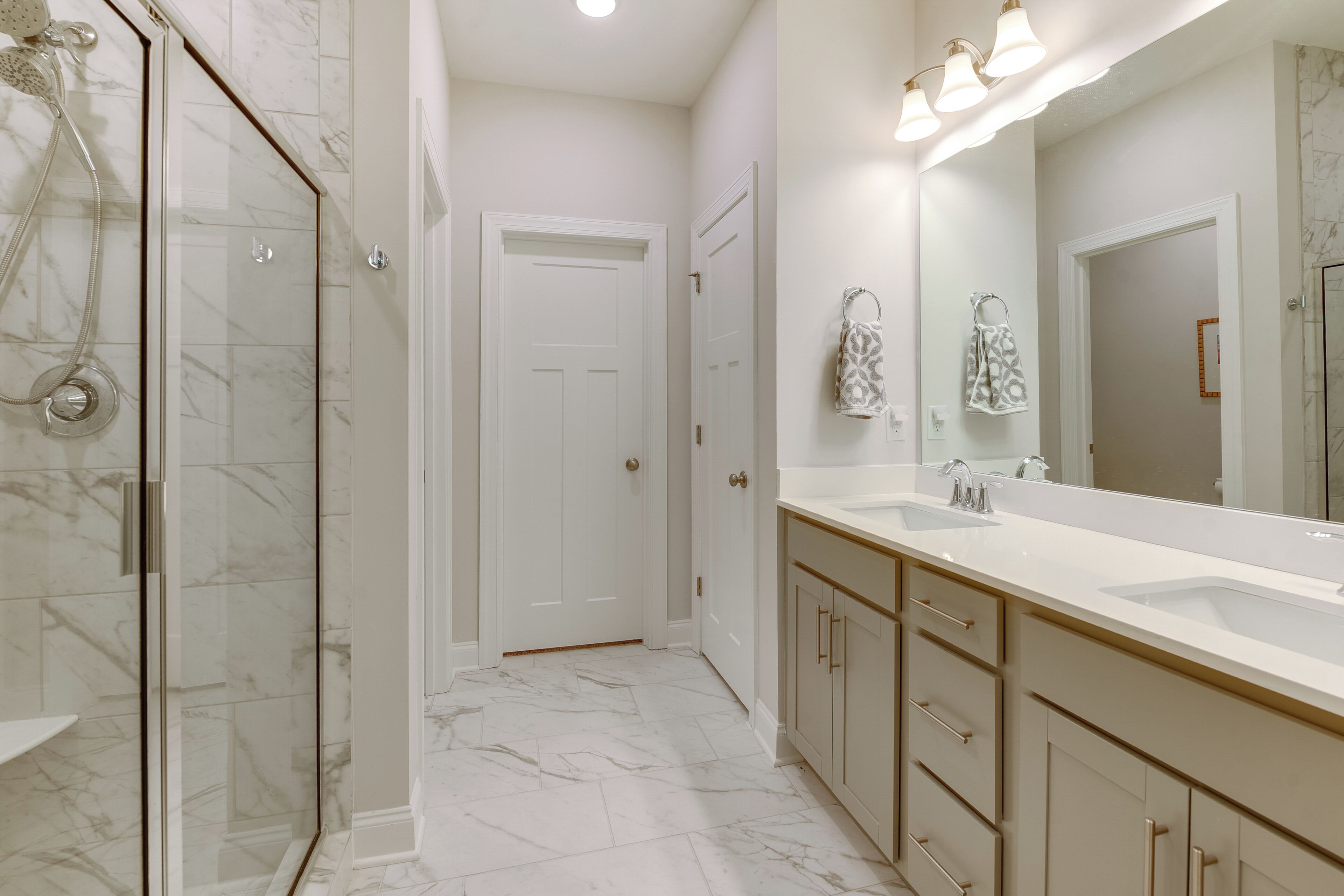Un baño moderno con ducha envuelta en vidrio, un espejo grande y un mueble de tocador doble.