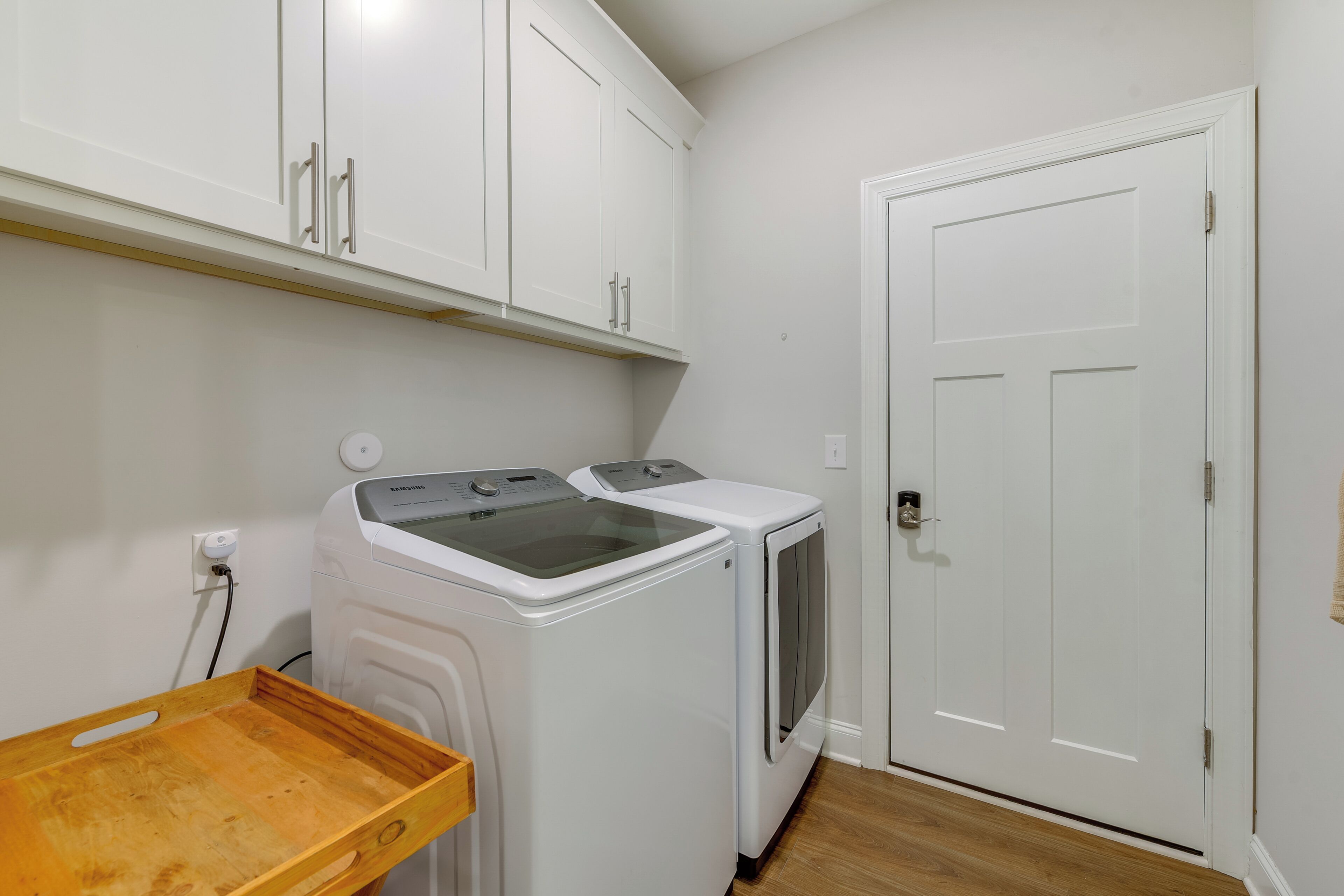 A laundry room with two white washing machines, a wooden drying rack, and a white door.