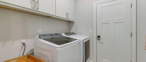 A laundry room with two white washing machines, a wooden drying rack, and a white door.