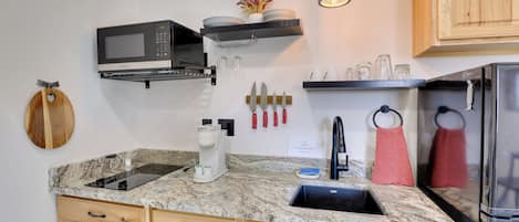 Una cocina con microondas integrado, cafetera y lavabo. Hay armarios de madera, un juego de cuchillos colgantes y una toalla colgada.