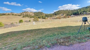 Ländliche Landschaft mit einem eingezäunten Feld, einer Kameraschwenkvorrichtung und hügeliger Kulisse.
