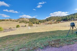 A rural landscape with a fenced field, a tripod-mounted camera, and a hilly backdrop.