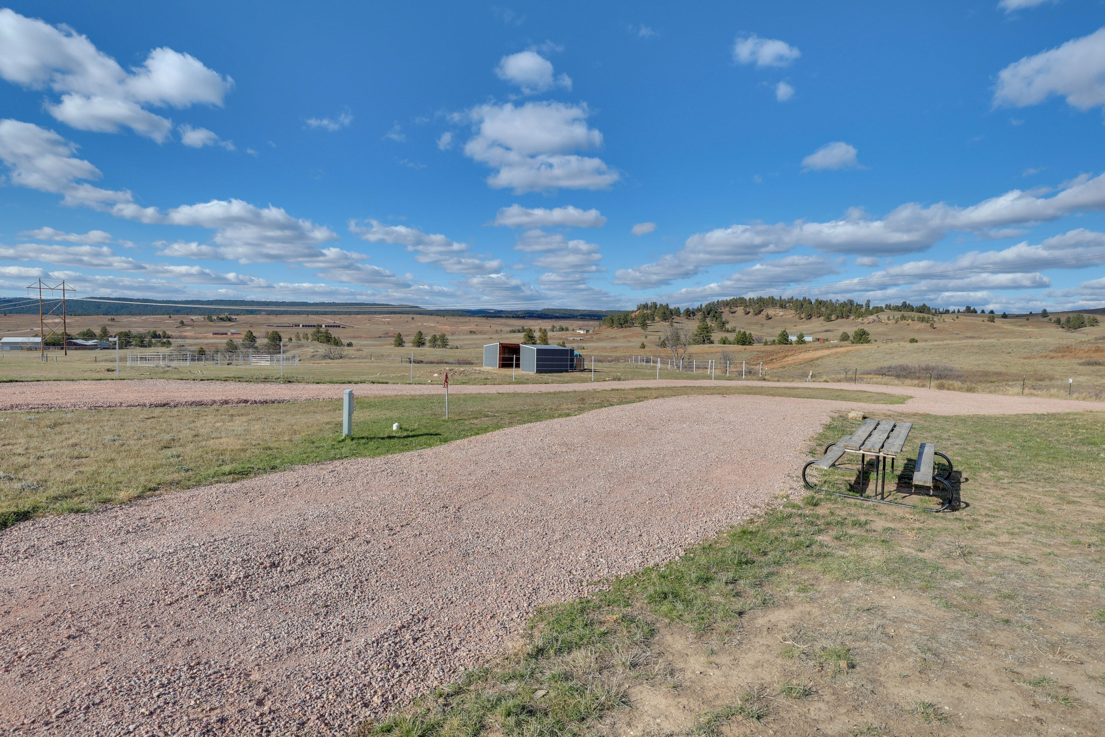 A gravel path leading to a fenced area with a bench and a small building.